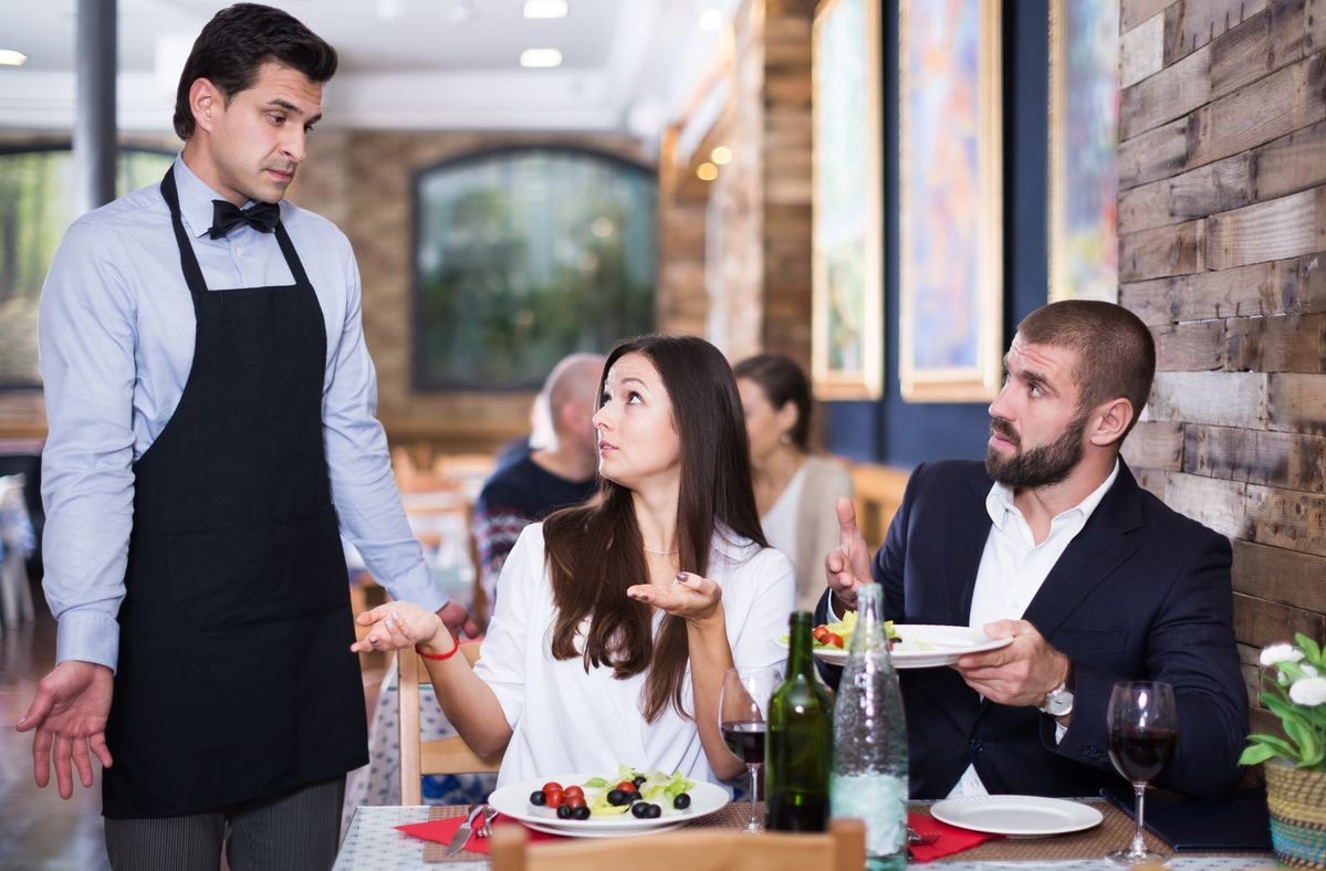 Casal discutindo com garçom em restaurante, indicando problema com prato ou serviço